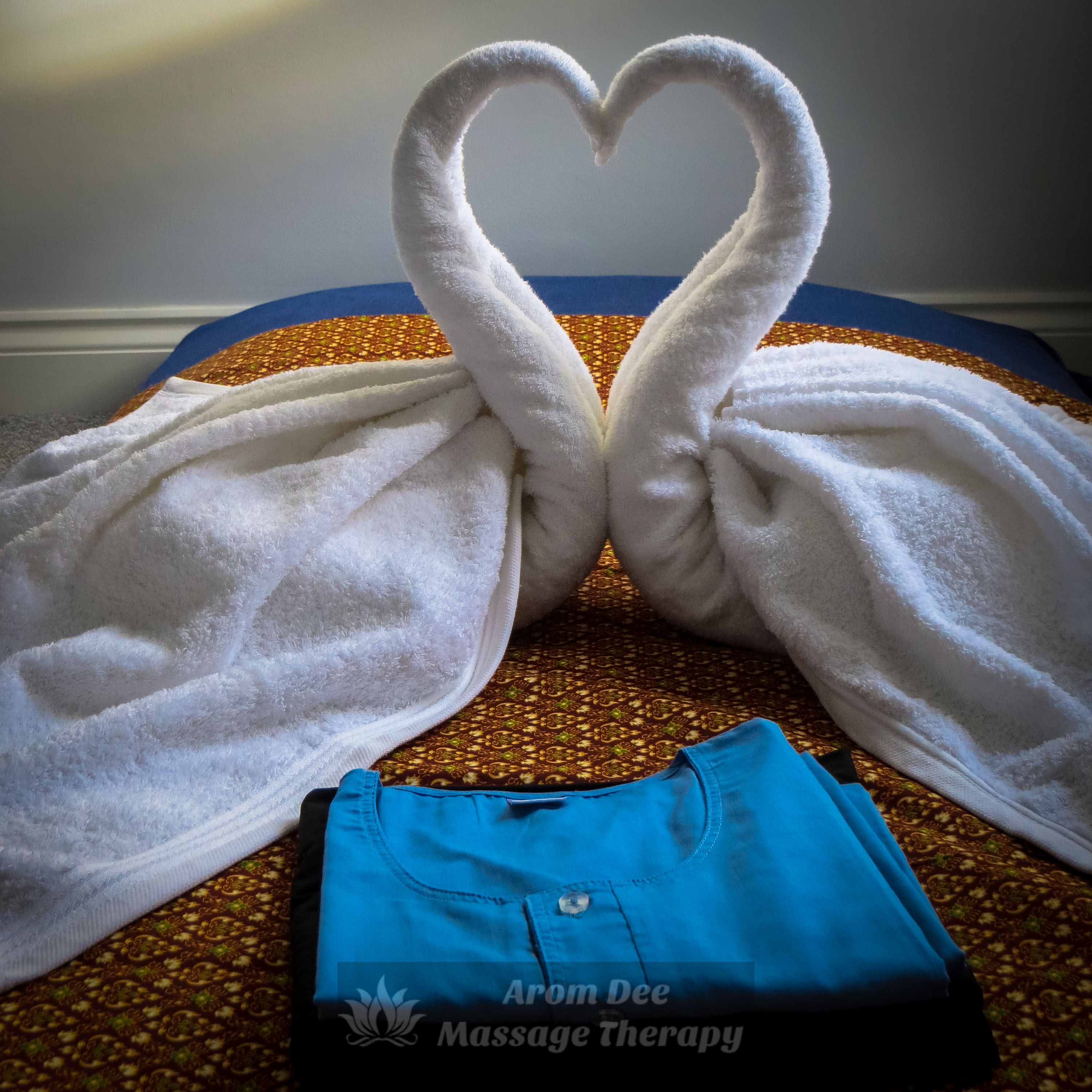 Folded client's pyjamas and two towels shaped as swans in heart on Thai massage mattress pad on floor